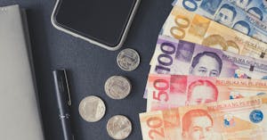 Flat lay of Philippine peso bills, coins, smartphone, and notebook. Ideal for financial themes.